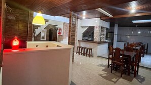 A spacious kitchen with a wooden ceiling, a central island, and a dining area with wooden chairs and stools. - Pousada Territorial  (Cairu)