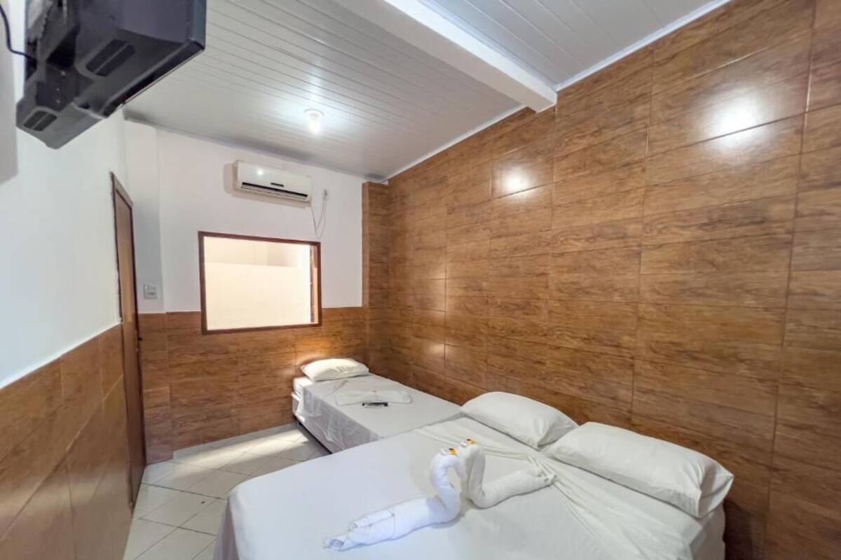 Ein Hotelzimmer mit zwei Betten, Holzvertäfelung an den Wänden, einem Wandfernseher und einer Klimaanlage.