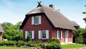 Une maison en briques rouges, avec des volets blancs et un toit de chaume.