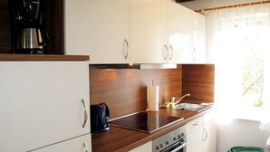 Une cuisine compacte avec des meubles blancs, un plan de travail en bois, une machine à café, une bouilloire et un évier.