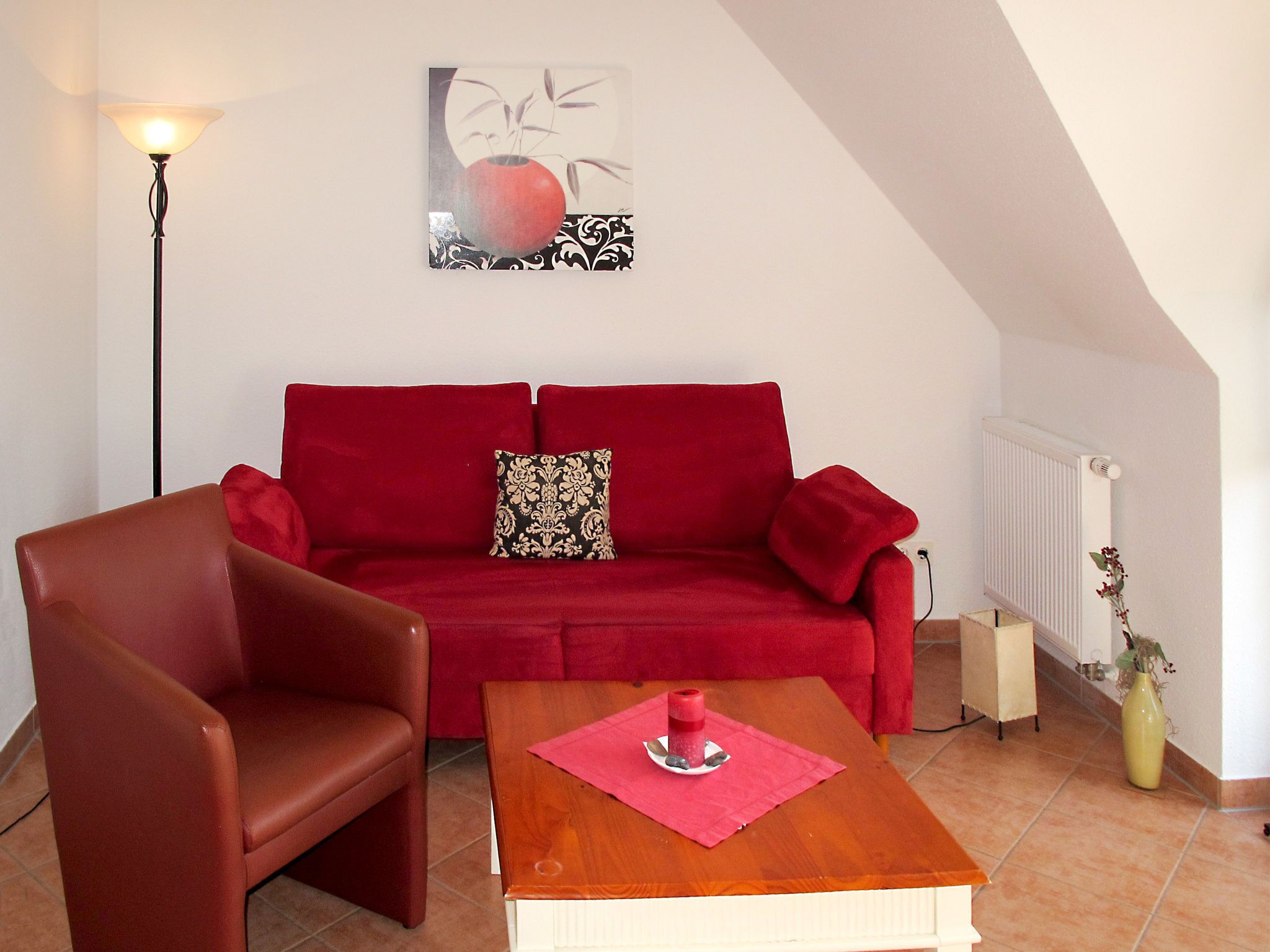 A red sofa with patterned cushions, a wooden coffee table, a floor lamp, and a wall-mounted artwork.