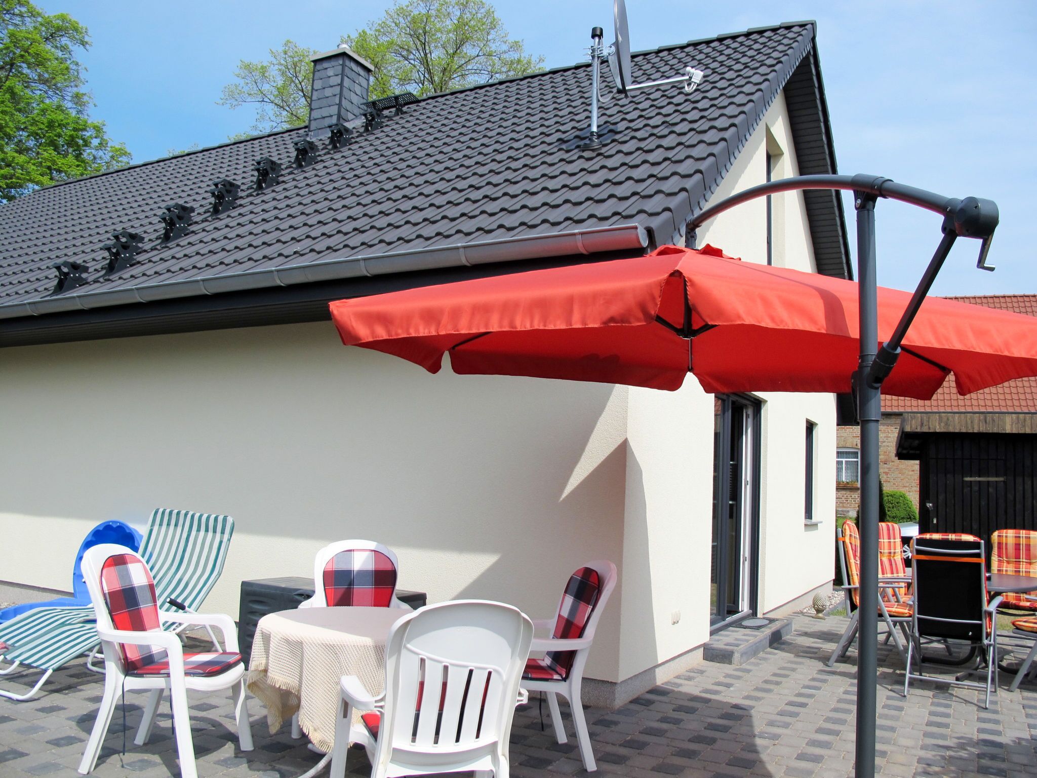 An outdoor patio with a table and chairs, a red umbrella, and a building with a tiled roof.