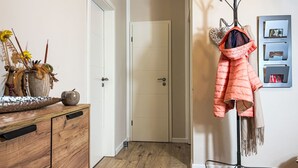 A hallway with a wooden dresser, a coat rack with a jacket, and a door leading to another room. - Johannika by Interhome (Godern)