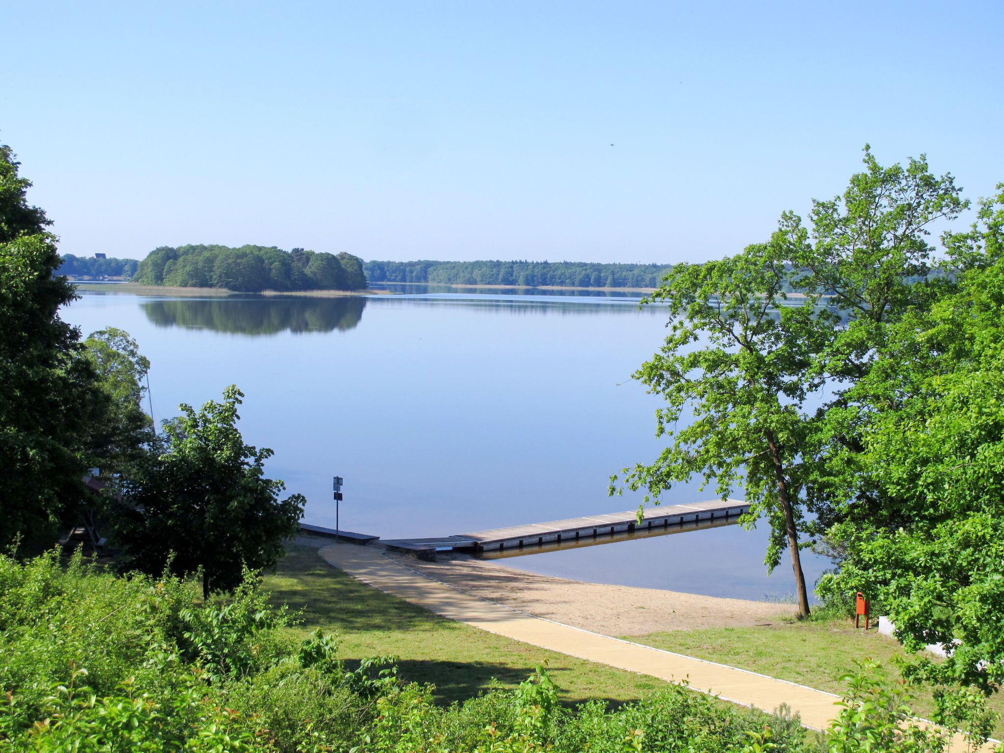 A tranquil lake with a dock extending into the water, surrounded by lush greenery and trees.
