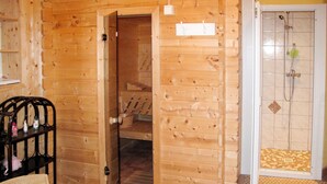 Interior de una cabaña de madera con puerta de madera, zona de ducha y una silla de mimbre.