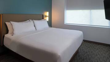 En pænt redt seng med hvide sengetæpper i et hotelværelse med teal vægge, et vindue og en vægmonteret lampe.