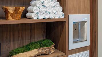 Una repisa de madera con un cuenco de madera, una pila de toallas enrolladas y un dispensador de agua blanco.