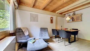 A room with a wooden ceiling, a dining table with chairs, a sofa, a small desk, and a window with curtains. - Fliederweg by Interhome (Siegsdorf)