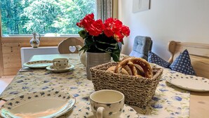 A dining table set with plates, a cup, a basket of pretzels, and a vase of red flowers. - Fliederweg by Interhome (Siegsdorf)