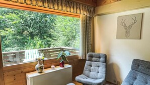 A cozy room with a wooden ceiling, a window with a view of greenery, two grey upholstered chairs, a small table with a vase and a book, and a framed artwork on the wall. - Fliederweg by Interhome (Siegsdorf)