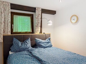Ein Schlafzimmer mit einem Bett, einem Fenster mit Vorhängen, einer Wanduhr und einer Nachttischlampe.