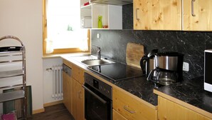 Et køkken med træskabe, en bordplade i sort sten, en stålvask, en kaffemaskine og et vindue med gardiner.