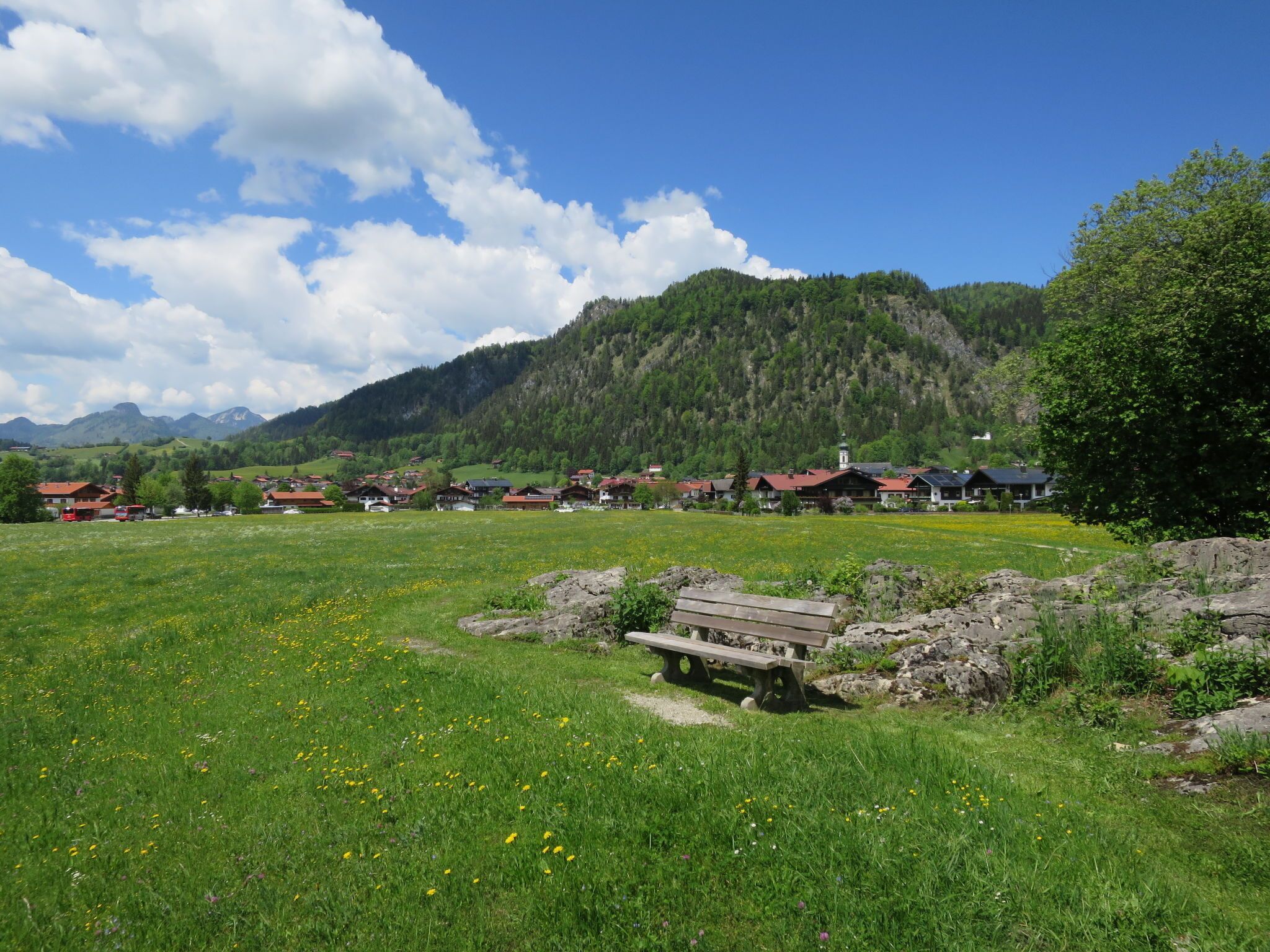 Un village rural avec des maisons traditionnelles, un banc en pierre et une chaîne de montagnes en arrière-plan.
