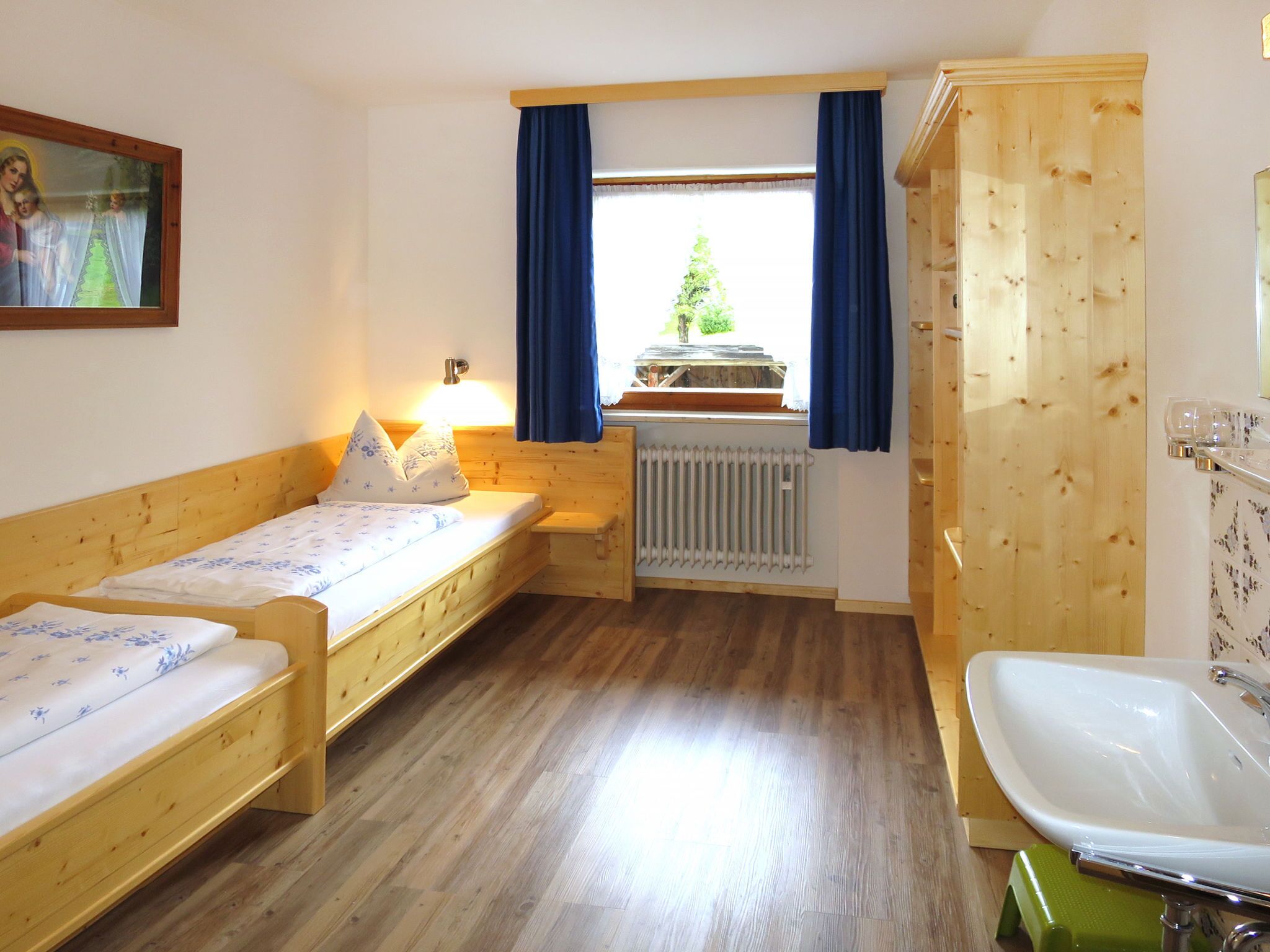 Ein kleiner, gemütlicher Raum mit zwei Holzbett, einem Heizkörper, einem Fenster mit Vorhängen und einem Holzschrank.