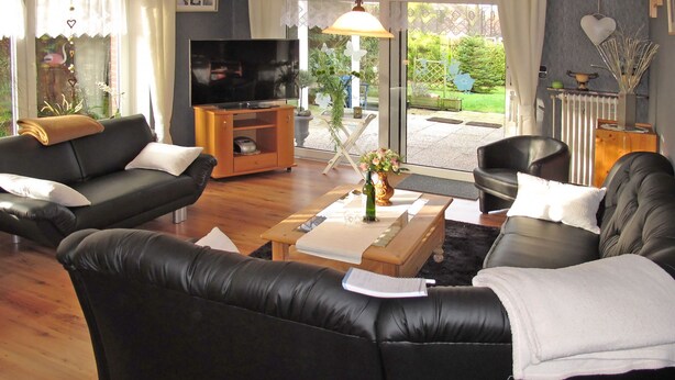 Un salon avec deux canapés en cuir noir, une table basse en bois, un téléviseur et une vue sur le jardin, visible à travers une porte vitrée.