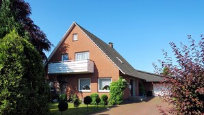 Une maison à deux étages avec une façade en briques, un balcon au premier étage et une allée pavée.