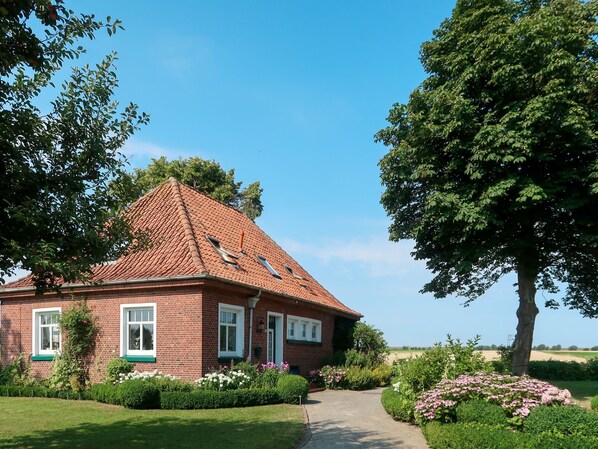 A brick house with a red-tiled roof, surrounded by a well-maintained garden with various plants and flowers.