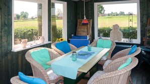 Zona pranzo con sedie in vimini, un tavolo con tovaglia blu e ampie finestre che si affacciano su un campo e alberi.