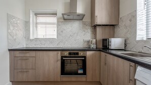 Une cuisine avec des meubles de rangement en bois, un four encastré, un four à micro-ondes et une fenêtre avec des stores.