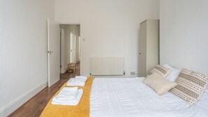 Une chambre à coucher avec un lit, un radiateur, un miroir et un couloir menant à une autre pièce.