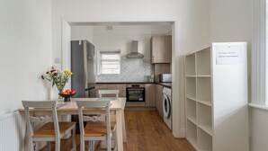Une cuisine compacte comprenant un coin repas, un four encastré, un lave-linge et un réfrigérateur blanc muni d’une étiquette indiquant le mot de passe Wi-Fi.