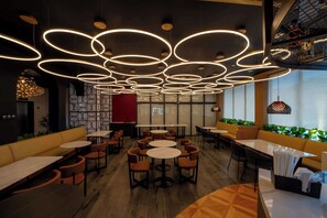 En modern restauranginteriör med runda bord och orange sittplatser, med en unik takdesign som inkluderar cirkelformade lampor.