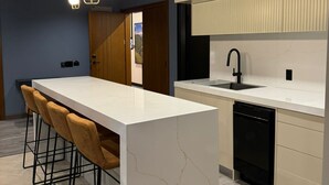 Een moderne keuken met een centraal eiland, barkrukken, hanglampen en uitzicht op de buitenruimte.