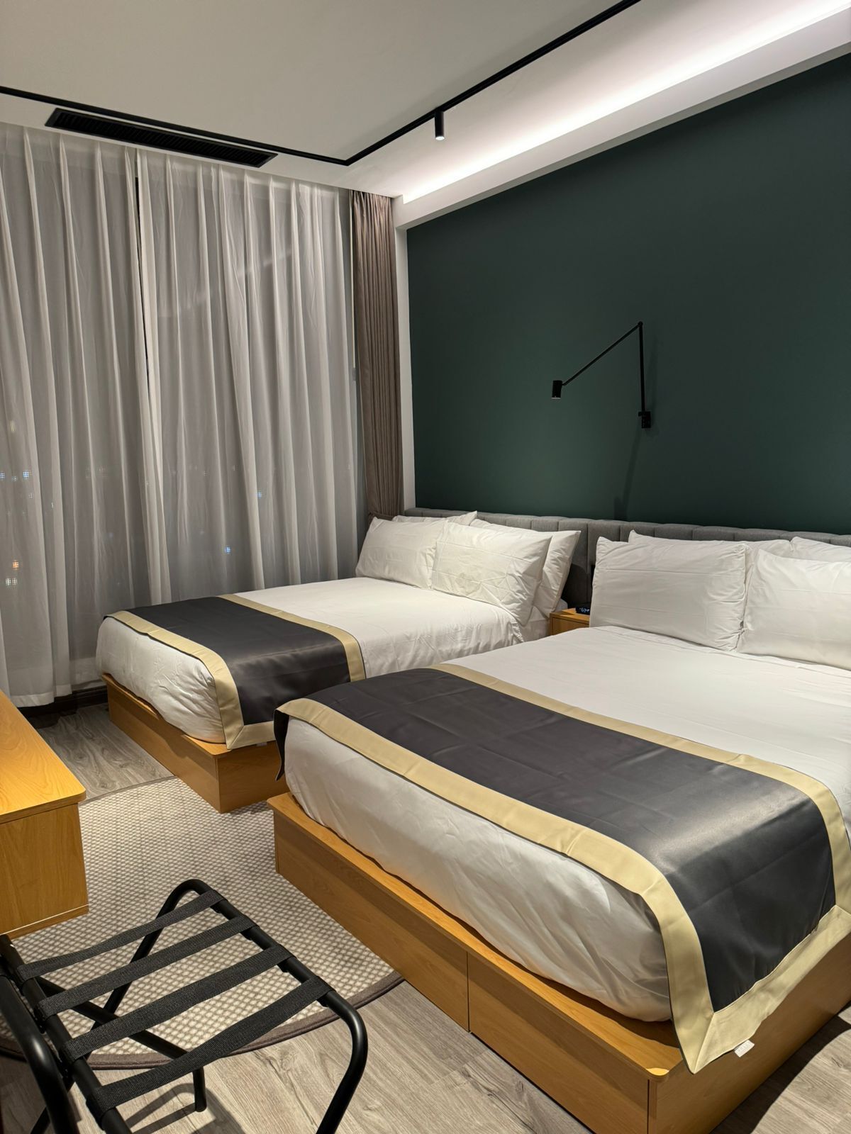 A hotel room with two beds, a desk, a chair, and a large window with curtains.