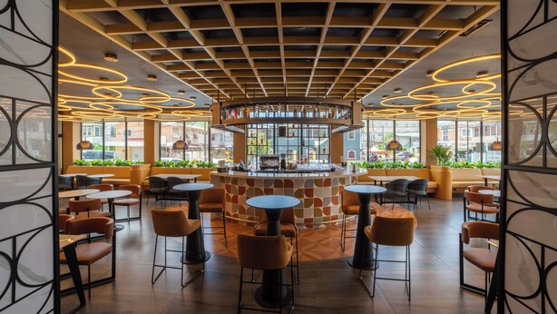Een modern café met een centrale bar, ronde tafels en oranje stoelen.