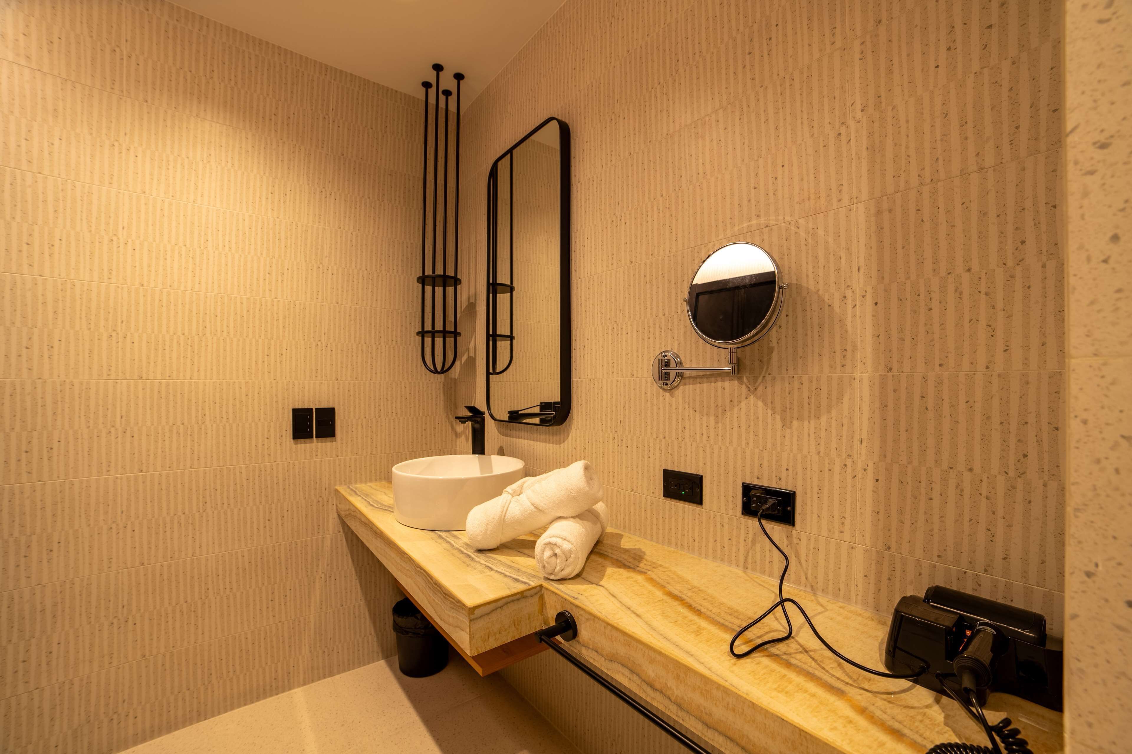 Une salle de bain moderne avec un meuble-lavabo en bois, un lavabo blanc, un porte-serviettes, un miroir et un sèche-cheveux branché.