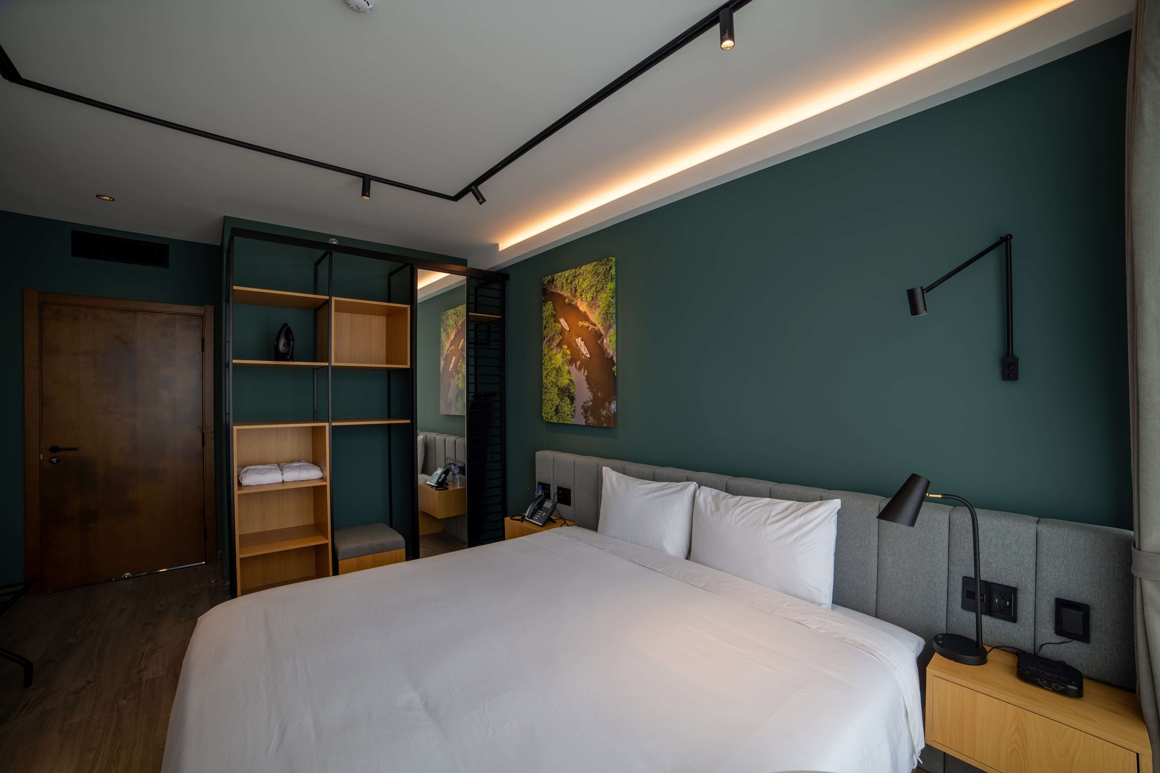 Une chambre d’hôtel moderne avec un grand lit, une armoire en bois, un bureau avec une lampe et un tableau au mur.