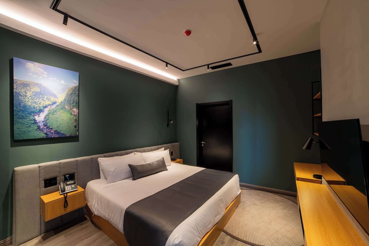 Ein modernes Hotelzimmer mit einem großen Bett, einem Nachttisch mit Telefon, einem Schreibtisch mit Stuhl, einem Bild an der Wand und einer Tür.
