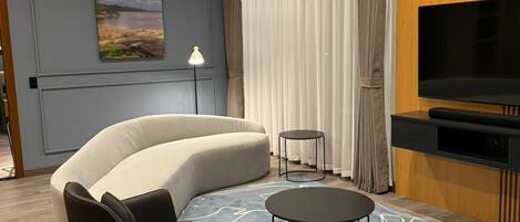 A modern living room with a curved sofa, two black armchairs, a round coffee table, and a flat-screen TV.