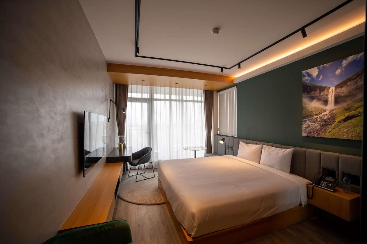 Ein modernes Hotelzimmer mit einem großen Bett, einem Schreibtisch, einem Stuhl, einem Fernseher und einem Bild eines Wasserfalls.