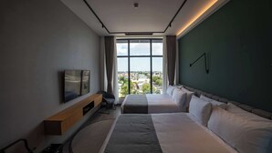 Een hotelkamer met twee bedden, een televisie, een bureau en uitzicht op de stad.