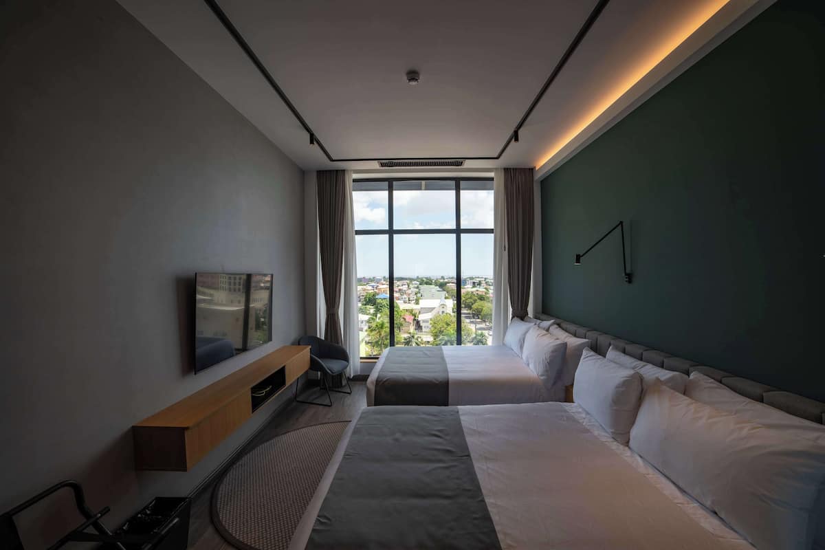 Ein Hotelzimmer mit zwei Betten, einem Fernseher, einem Schreibtisch und Blick auf die Stadt.