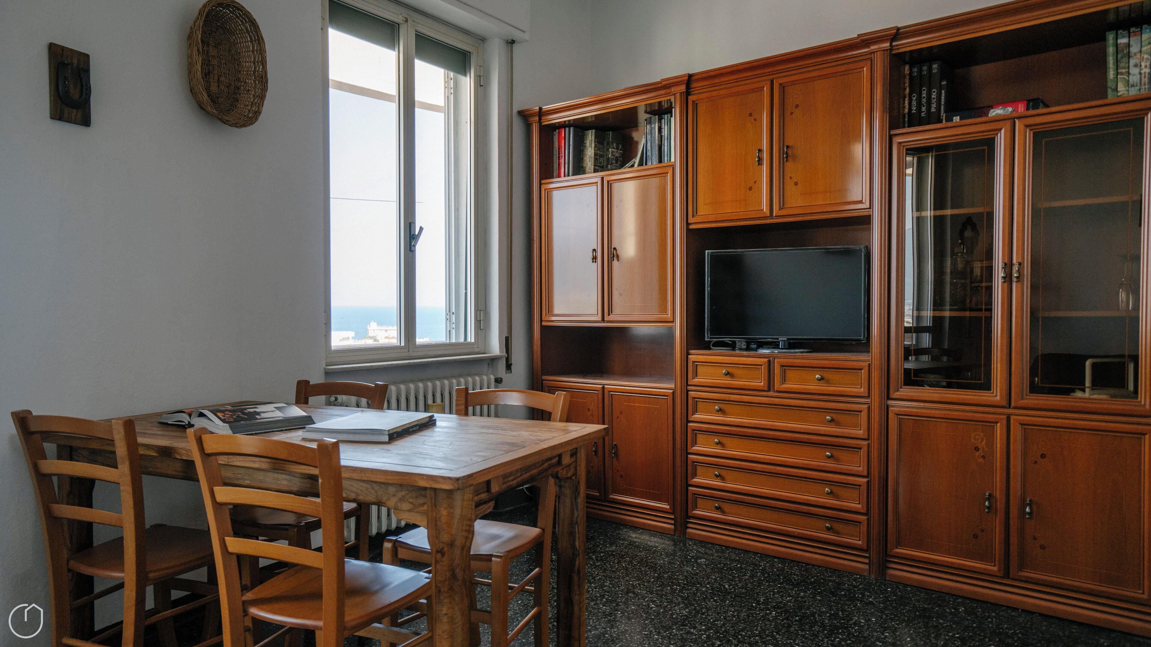 Ein Zimmer mit einem Holzesstisch, Stühlen, einem Fernseher auf einem Schrank und Bücherregalen.