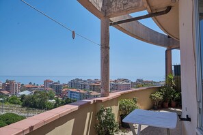 Un balcone con vista sulla città costiera, piante in vaso e ringhiera in metallo.