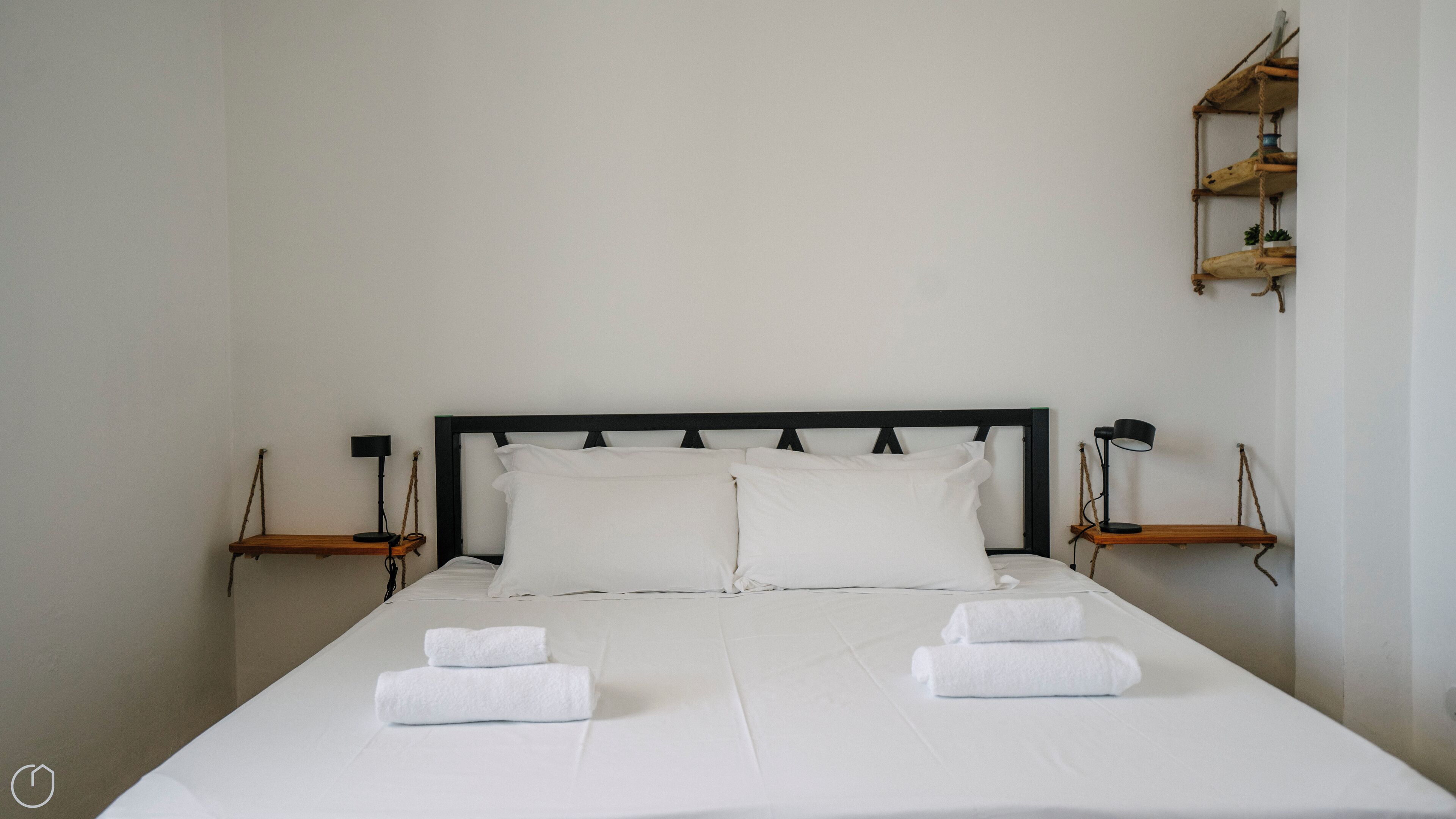Un lit bien fait, avec du linge de lit blanc et deux serviettes, une tête de lit noire et des tables de chevet avec des lampes.