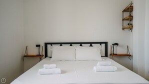 Een opgemaakt bed met witte lakens en twee handdoeken, een zwart hoofdbord en nachtkastjes met lampen.