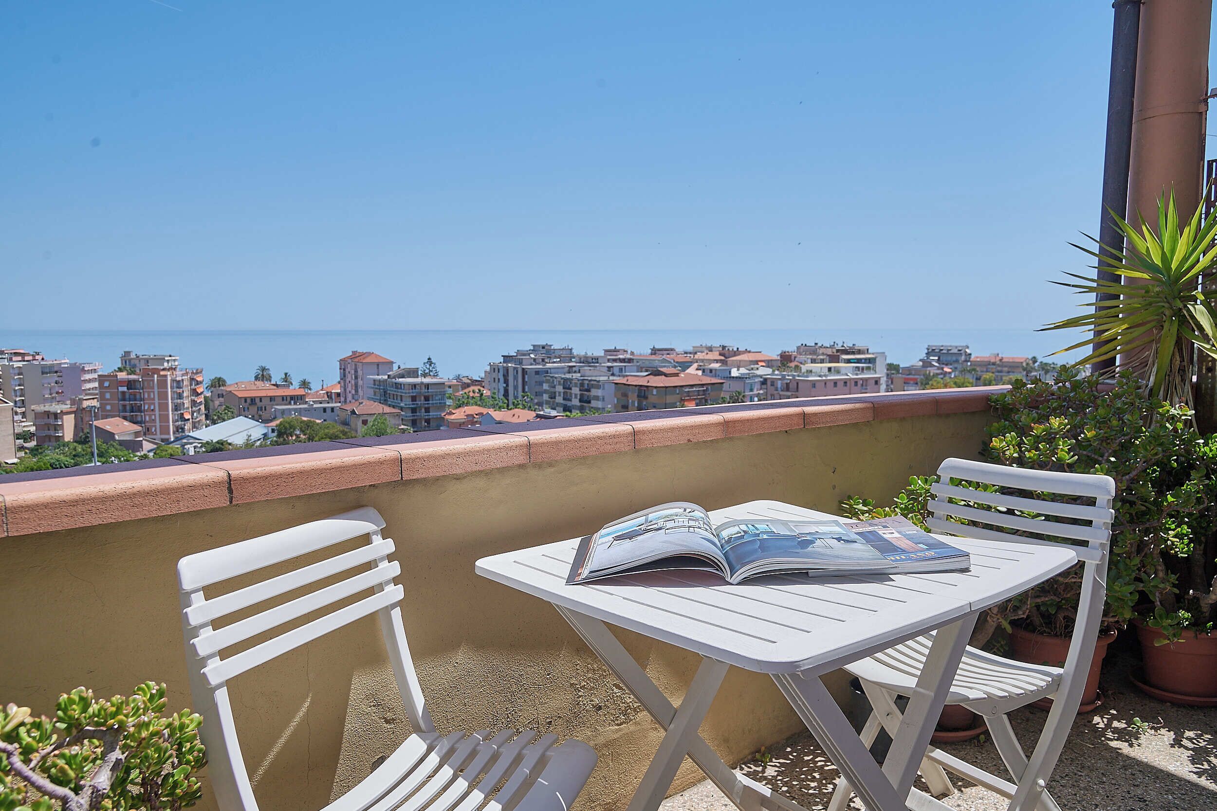 A balcony with a table and chairs, a magazine, and a view of the cityscape.