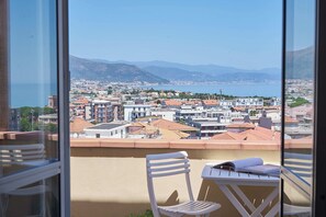 A balcony with a view of a coastal town, a chair, and a table with a book. - Tra le Nuvole - Two Bedroom Apartment, Sleeps 5 (Albenga)