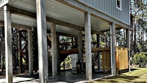 A two-story house with a covered porch supported by concrete pillars, surrounded by a grassy yard and trees.