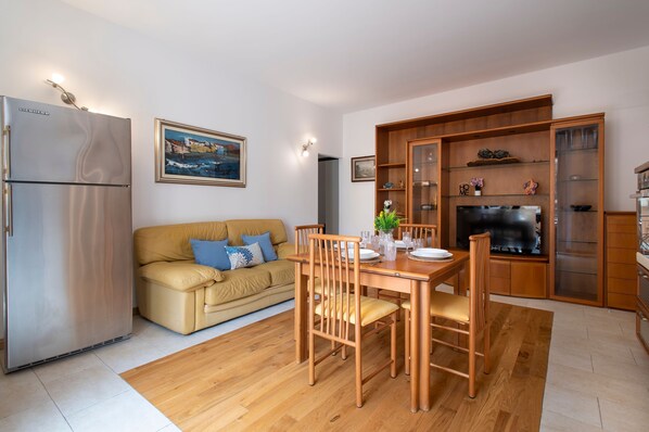 Un espace de vie compact comprenant un coin cuisine, un coin repas avec des meubles en bois, un canapé avec des coussins et un tableau accroché au mur.