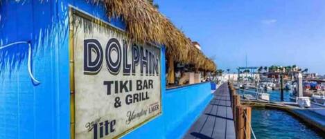 A Dolphin Tiki Bar & Grill with a thatched roof and a view of the marina.