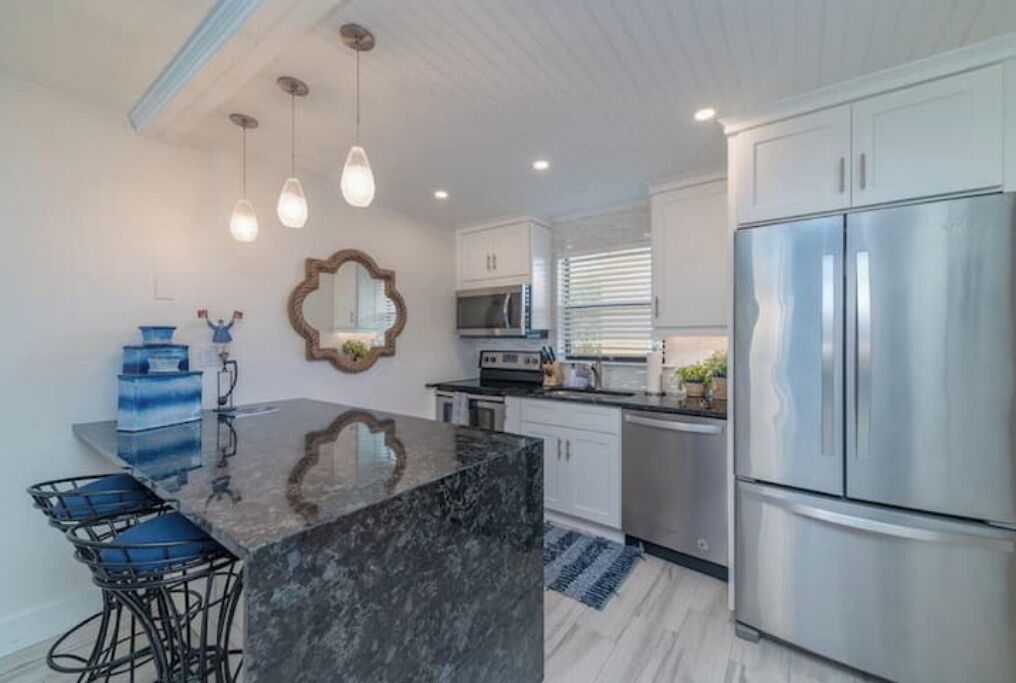 A modern kitchen with a marble island, stainless steel appliances, and pendant lighting.