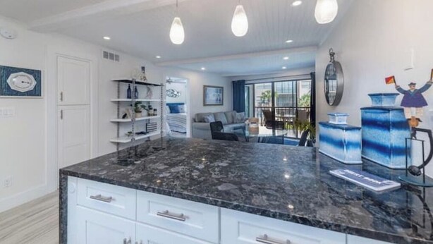 A modern kitchen with a granite countertop, white cabinetry, pendant lighting, and a view to the living area. - Beautiful modern gulf coast condo  Marco Island, FL (Marco Island)