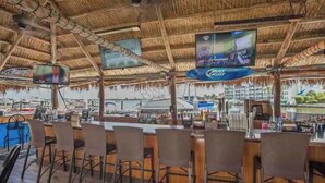 An outdoor bar area with thatched roof, bar stools, and a TV screen displaying a program. - Beautiful modern gulf coast condo  Marco Island, FL (Marco Island)