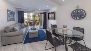 A living room with a sofa, a coffee table, and a dining area with chairs and a table. There is a large clock on the wall. - Beautiful modern gulf coast condo  Marco Island, FL (Marco Island)