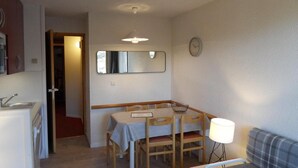 Ett kompakt kök med en diskho och en matplats med ett bord och stolar. Det finns en spegel på väggen ovanför bordet och en klocka på väggen till höger.